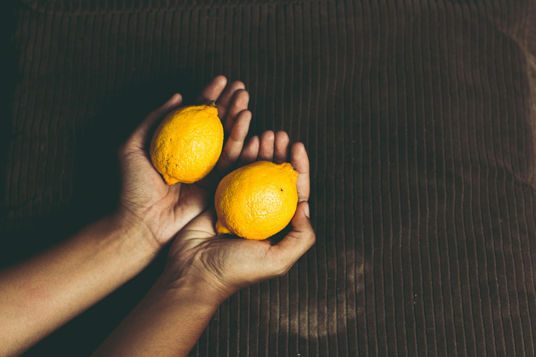 Two fresh lemons held in cupped hands on a brown surface, symbolizing renewal and gentleness.