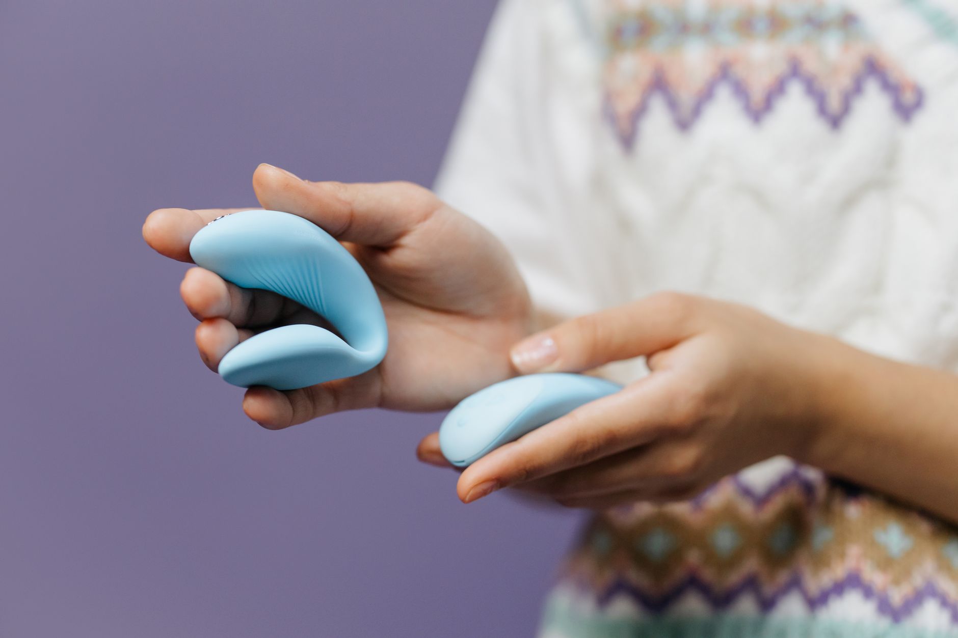 Hand holding a blue clitoral vibrator against a purple background, representing sensory reset and renewed pleasure.
