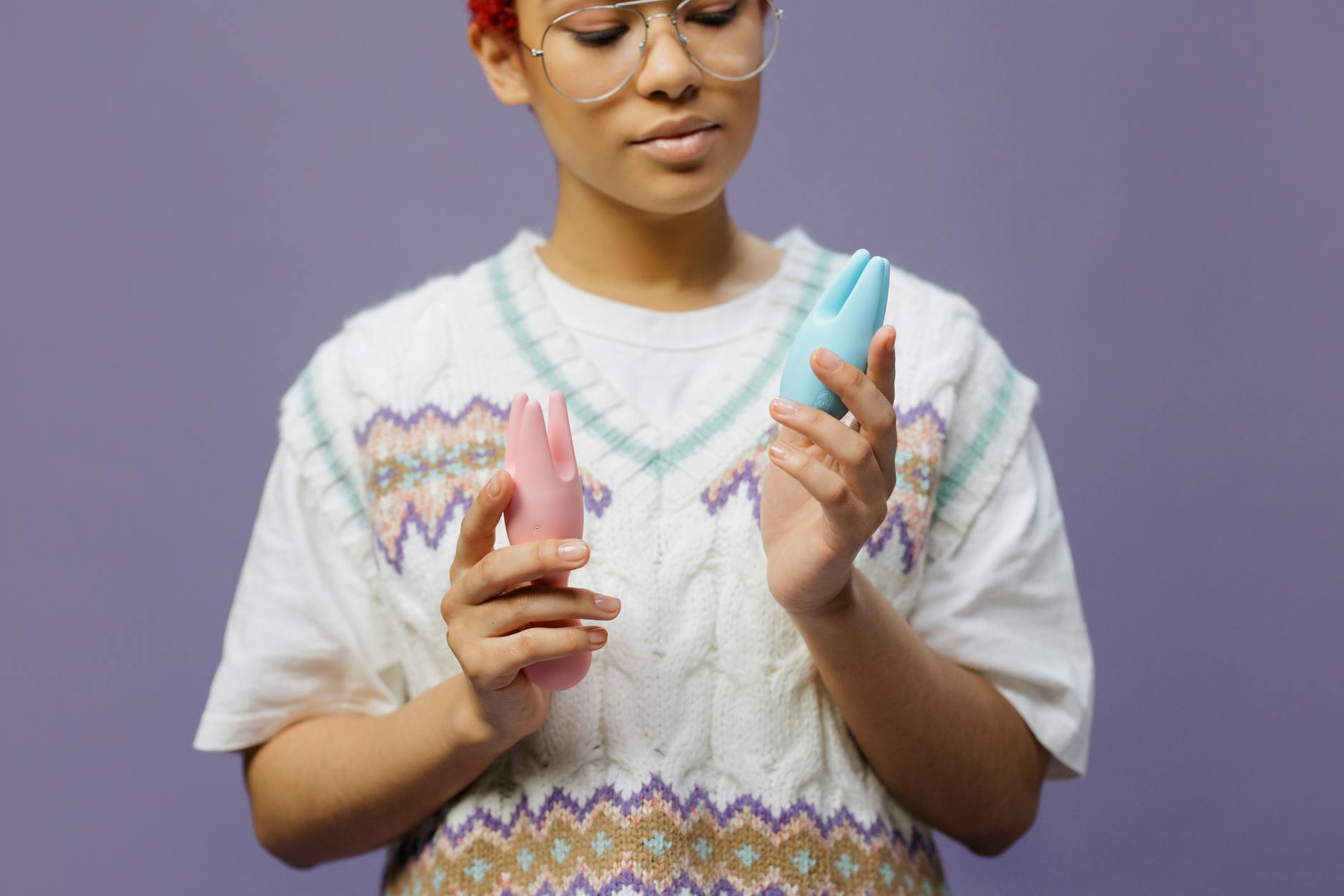 Woman in eyeglasses holding contemplative expression while holding blue and pink silicone toys