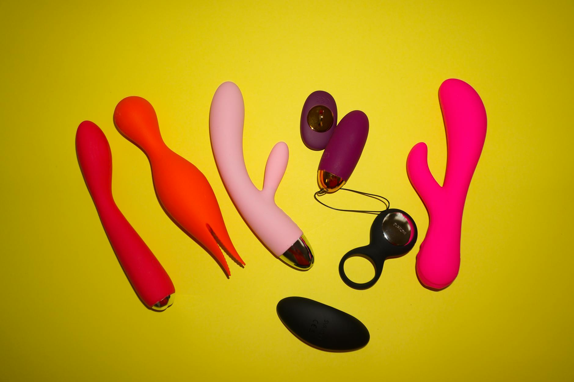 Colorful modern vibrators arranged on bright yellow background, showcasing various intimate wellness tools